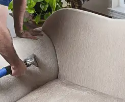 Professional upholstery cleaner deep-cleaning a fabric sofa with a handheld extraction tool and hose in Dallas, TX.